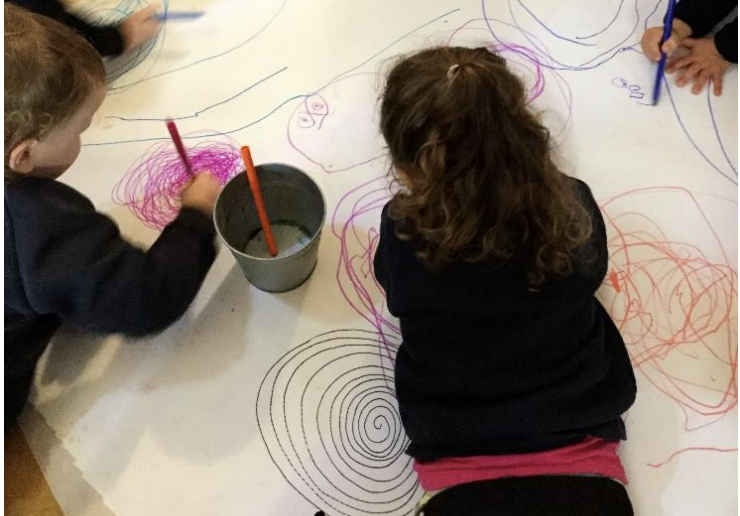 Children drawing spirals together on a large sheet of paper