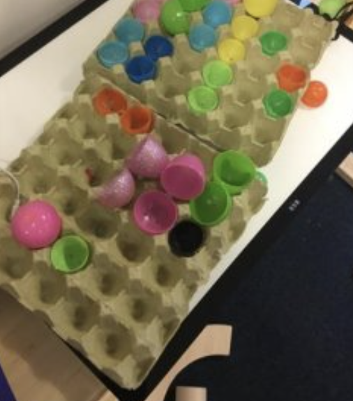 Two egg boxes, each with some plastic egg shells sitting in the holes