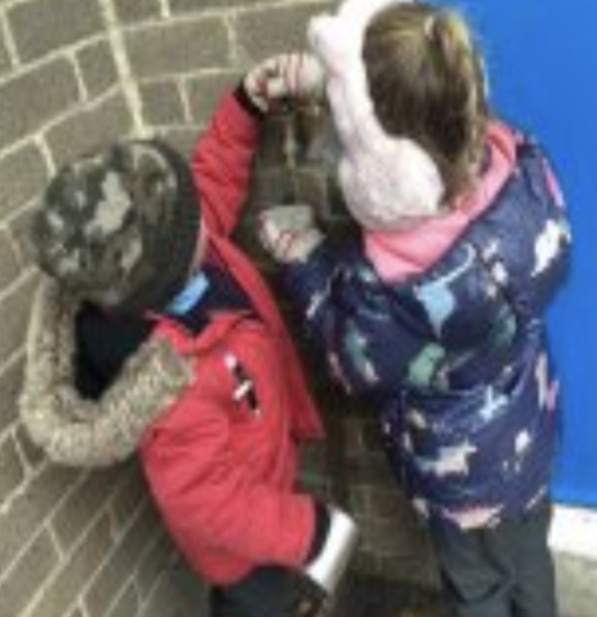 Two children filling a water bottle through a funnel at an outdoor tap