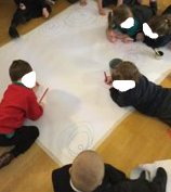 Children laying on the floor, drawing spirals and sets of concentric circles on a large piece of paper
