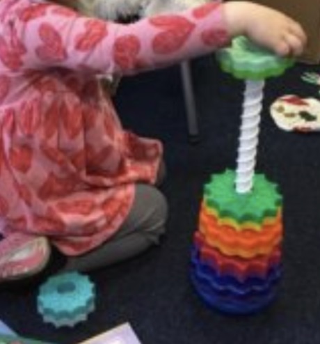A child stacking differently sized cogs onto a threaded pole, almost in size order.